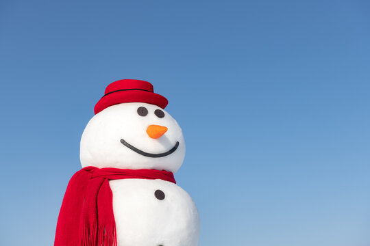 Funny snowman in stylish red hat and red scalf closeup on blue sky background