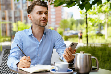 Bristle man using cellphone and writing down notes in cafe outdoors