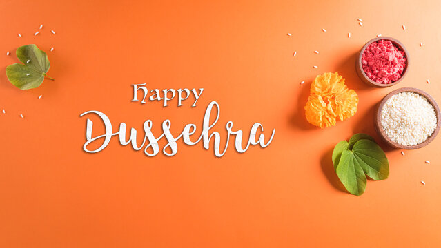 Happy Dussehra. Yellow flowers, green leaf and rice on orange background. Dussehra Indian Festival concept.