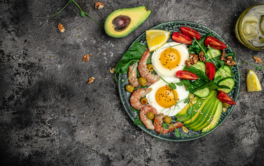 Ketogenic diet breakfast shrimps, prawns, soft fried egg, fresh salad, tomatoes, cucumbers and avocado on a dark background. Keto, paleo lunch. Top view