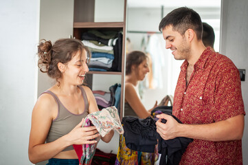 A charming young couple trying on clothes and having fun standing behind the wardrobe in the bedroom in their new apartment
