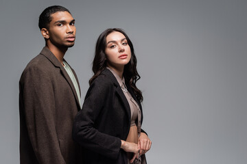 young african american man in woolen autumnal coat near stylish woman in black blazer isolated on grey.