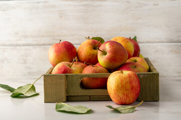 Close up of Yellow and red apples in wooden crate on light surface food harvest concept