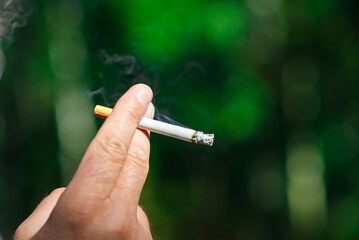 Mans hand smoking cigarette at summer day,closeup.Blurred outdoors green background.Copy space.