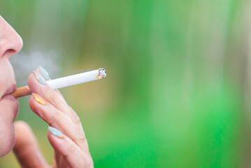 Middle age woman smoking cigarette at summer day,closeup.Blurred outdoors green background.Copy space.