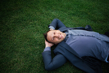 Happy Young businessman in a suit lying on the green grass and relaxing in park.