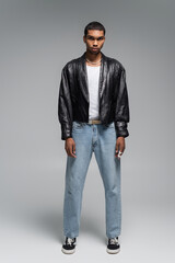 full length of young african american man in jeans and leather jacket on grey.