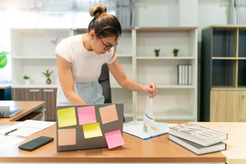 asian beautiful woman focus on business work. busy female worker working overtime try to find information on paper sheet and sticky notes on table. occupation office woman overwork alone at workplace