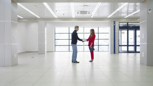 Man and a woman businesswoman shake hands in an empty hangar, the general plan. Successful negotiations business people shake hands and talk. Conclusion of a commercial partnership