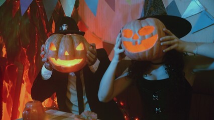 A guy and a girl in creepy costumes with a Jack-o'-lantern pose in front of the camera on Halloween