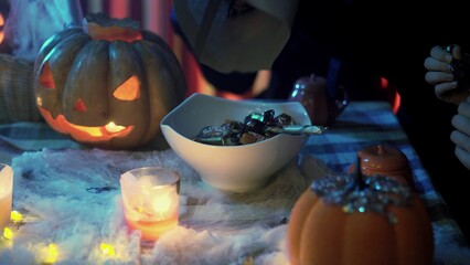 An unrecognizable person pours candy into a plate for Halloween. Creepy atmosphere. Trick or treat
