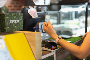 Woman paying bill through smartwatch using NFC technology in cafe.