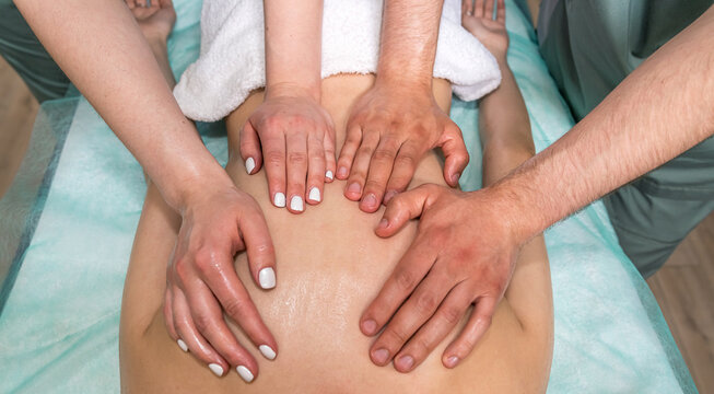 Two masseuses a man and a woman are giving a full body massage to a woman.
