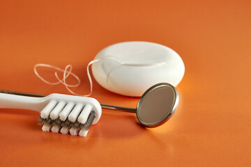 Dental mirror, dental floss and toothbrush on orange background. Dental care.