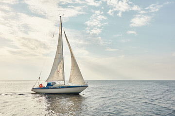 Fototapeta na wymiar White sloop rigged yacht sailing in the Baltic sea on a clear day. Transportation, cruise, yachting, regatta, sport, recreation themes. Travel, exploring, wanderlust concepts