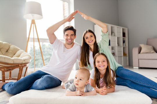 Photo of cheerful peaceful full family sitting arms make roof gesture toothy smile spend pastime house indoors