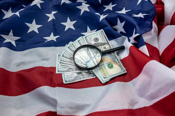 large amount of American dollars spread out with magnifying glass and wallet on the USA flag.