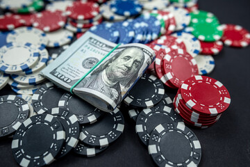 colored poker chips scattered with a roll of US dollars isolated on a black background.