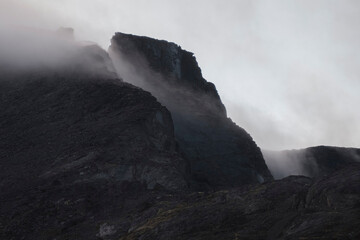 Harsh stone rocks in the clouds and fog in black mountains.