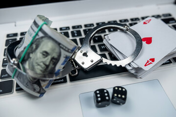 Handcuffs with dice on laptop keyboard isolated on black background.