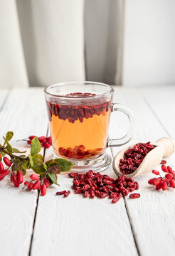 Berberis vulgaris also known as common barberry, European barberry or barberry tea drink in class mug in home kitchen. Dried and fresh berries for decoration on vintage white wood board background.