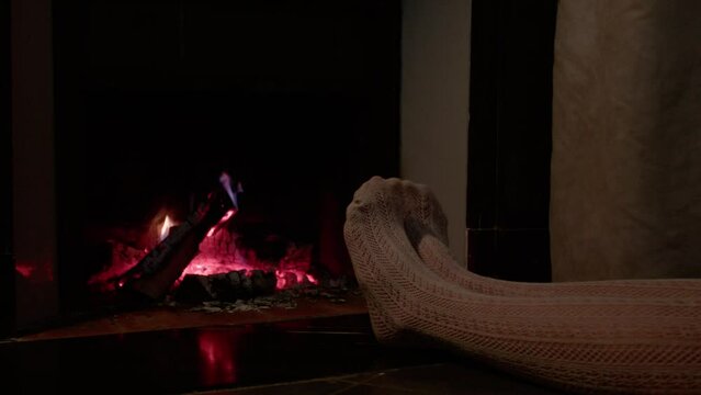Woman's legs in pantyhose getting warm from fireplace during winter night