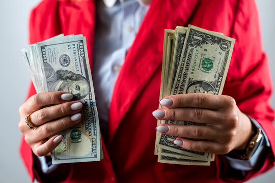 young woman in a red jacket showing a pile of money in dollars isolated on plain background