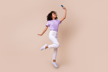 Fototapeta na wymiar Full length photo of sweet cute girl dressed purple t-shirt jumping high recording video vlog modern gadget isolated beige color background