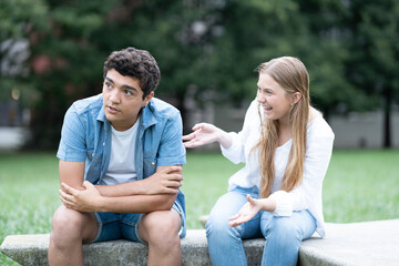 Bored teenager boy listening excited girl talking too much outdoors in a park