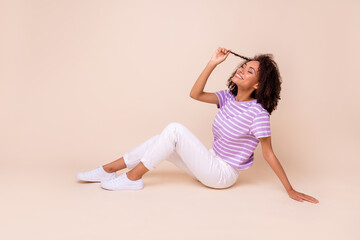 Photo of positive cheerful pretty girl with wavy hairstyle wear striped t-shirt sitting eyes closed isolated on beige color background