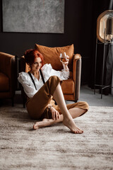 A beautiful girl in a white shirt and suspenders with a glass of wine. Posing