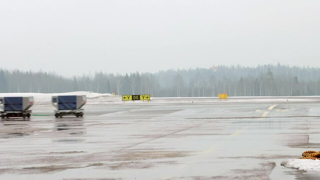 A vehicle pulls cargo carts at the snowy Helsinki Airport, Finland