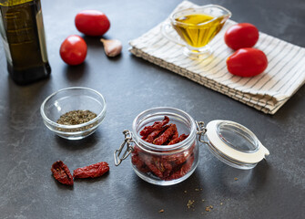 glass jar with sun dried tomatoes, spices and olive oil on dark background. Mediterranean cuisine.
