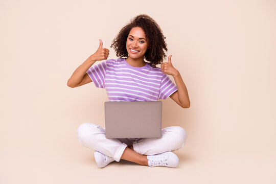 Photo of adorable lovely girl with brunette hair dressed striped t-shirt show like approve hold laptop isolated on beige color background