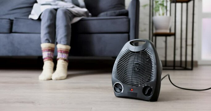 woman warming cold room with electric heater at home. heating season