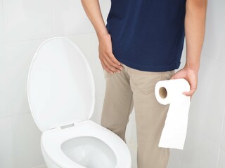Young man has diarrhea holding his bum on bathroom background and hemorrhoid. Closeup photo, blurred.
