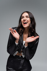excited young woman in stylish black leather jacket gesturing isolated on grey.