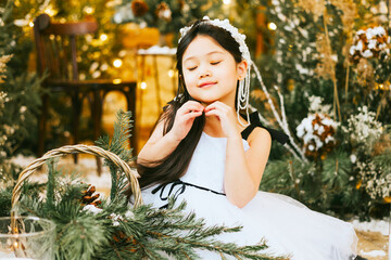 little beautiful asian girl in white dress and crown sit in loft room decorated with wooden...