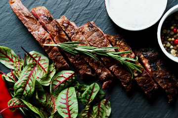 Sliced grilled steak medium rare served on black cutting board with vegetables. Delicious juicy...