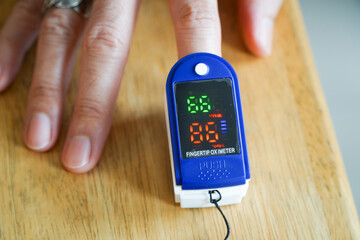 Asian man hands using modern fingertip blood oxygen meter on wooden table,closeup