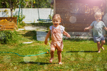 Two happy little children boy, girl run around water sprinkler - obrazy, fototapety, plakaty
