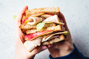 Turkey and apple sandwich in hands, gray background. Thanksgiving leftovers concept.