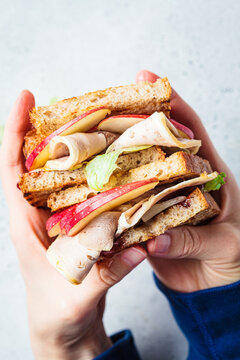 Turkey and apple sandwich in hands, gray background. Thanksgiving leftovers concept.