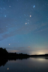 Autumn night landscape under starry sky. Stars reflecting from calm water surface.