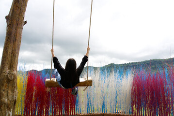 Back of Asia girl in black playing swing with the clouds sky and colorful dry tree from Thailand.