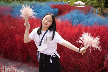 An Asia girl wearing a white T-shirt, black skirt holding pink flowers and dancing with a background of colorful dry trees from Thailand.