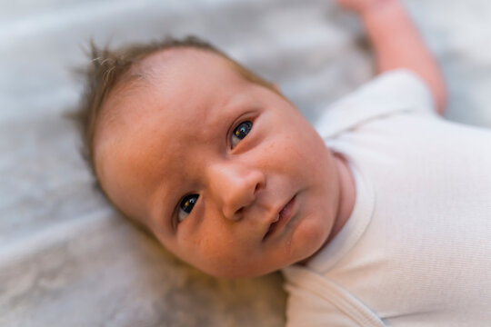 Close-up portrait of caucasian newborn baby boy lying on his bank on blanket on the floor wearing white t-shirt looking into camera. Horizontal shot. High quality photo