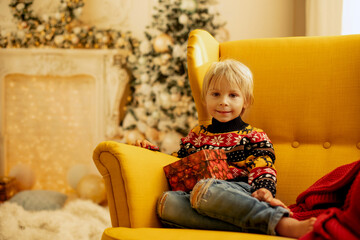 Cute blond toddler preschool boy, eating cookies and opening present on Christmas on cozy home