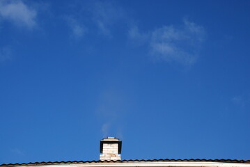 Chimney against the blue sky. The white brick chimney of the spherhu stove is covered with an iron...