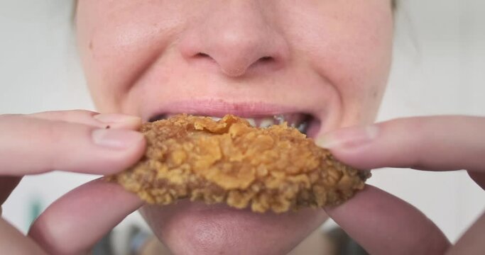 Young woman with braces eats fast food, fried chicken wings. Close-up, chewing mouth. Pleasure from junk food, satisfying hunger.